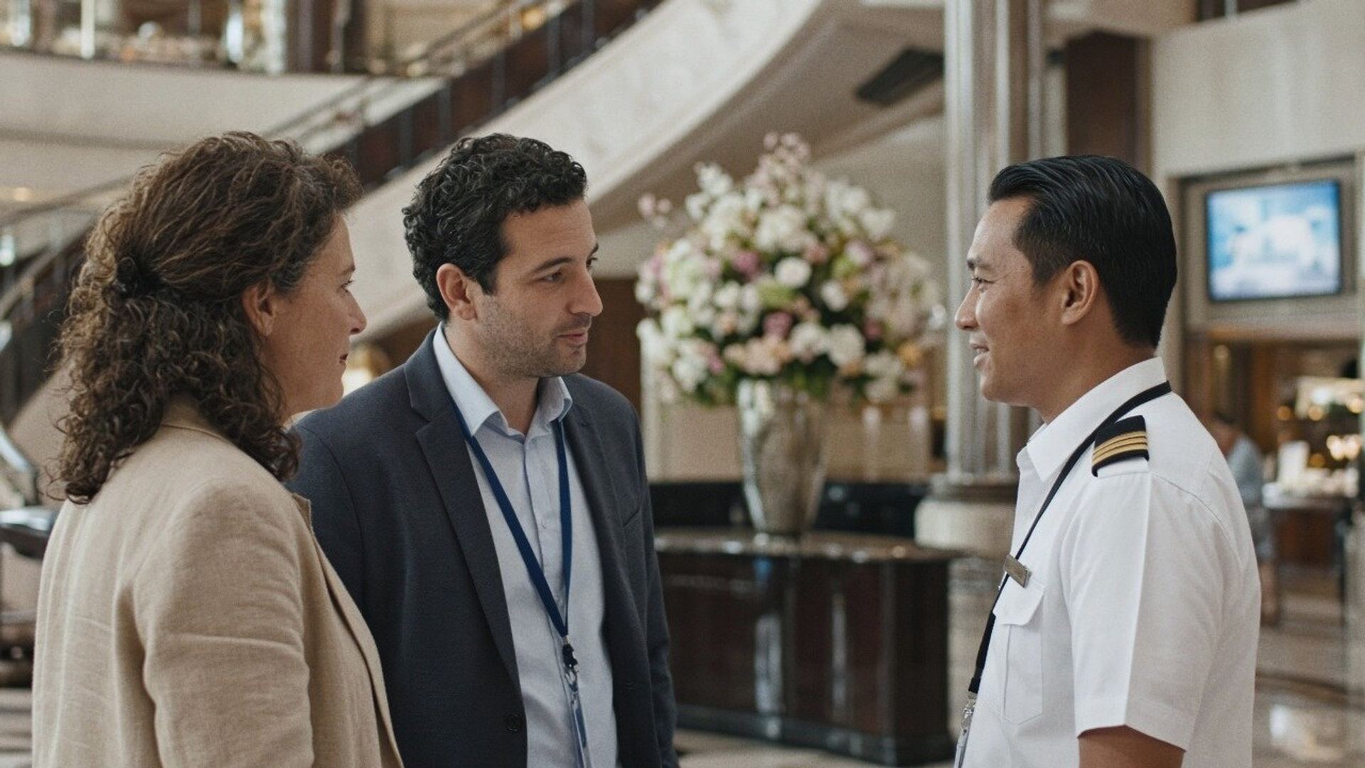Two advisors talk with a cruise ship officer in the ship's atrium.