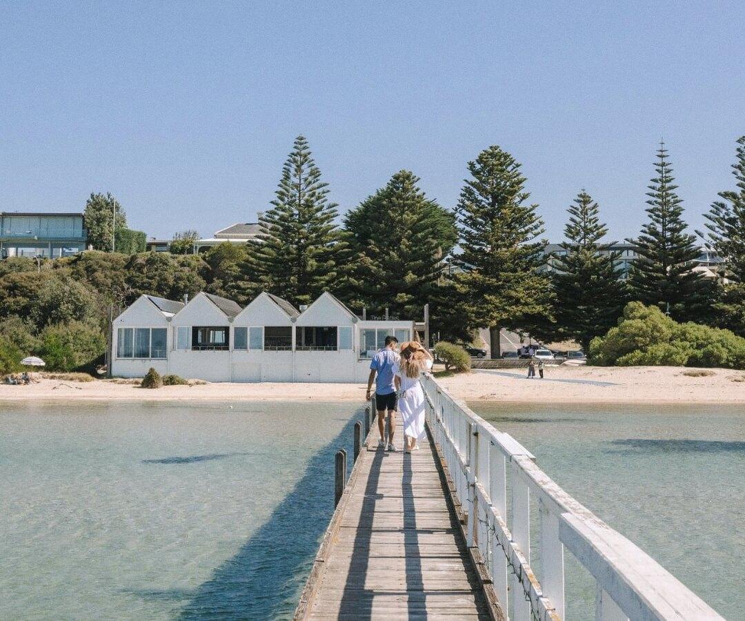 A jetty leading back to the beach at Sorrento, Victoria, with bathing boxes and pines behind